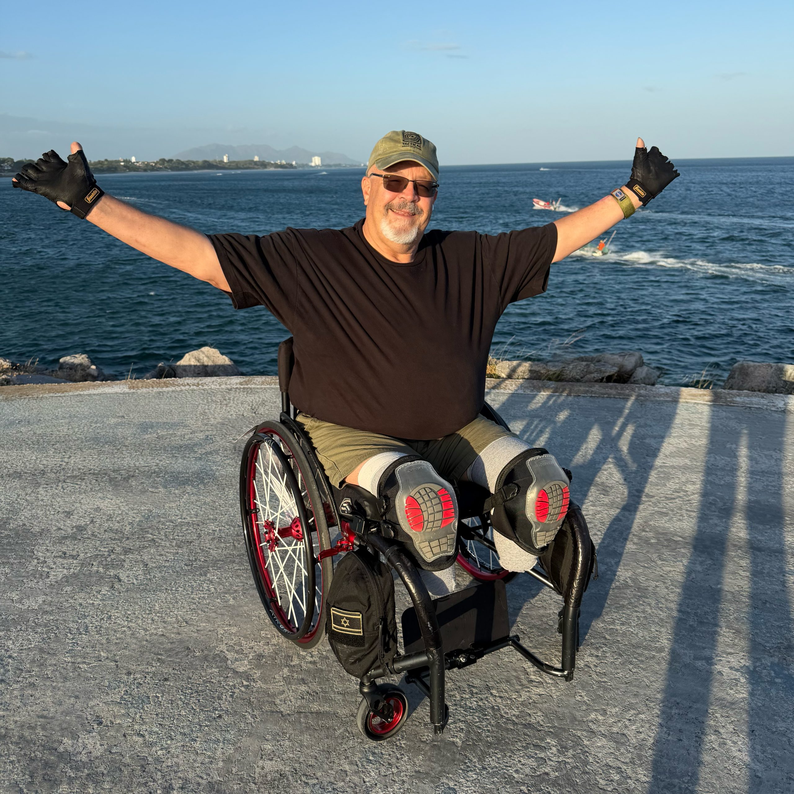 James Lea in his wheelchair, arms wide, on a waterfront in Panama