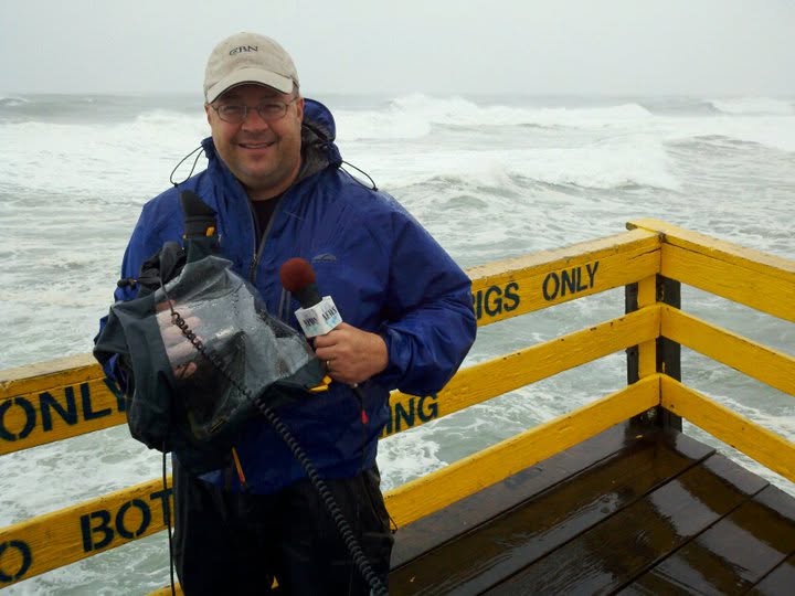 James on a seawall in a hurricane with a broadcast camera and microphone